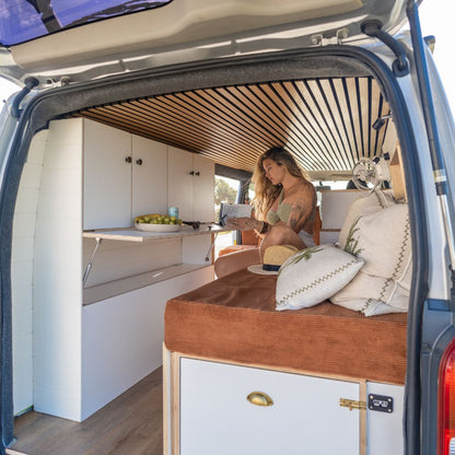 Peaceful van-life moment — girl reading on the side of a sliding bed in a cozy campervan with high storage units.